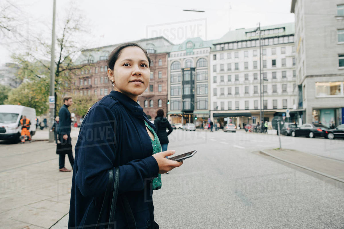 Side view of female entrepreneur with phone standing in city Royalty-free stock photo