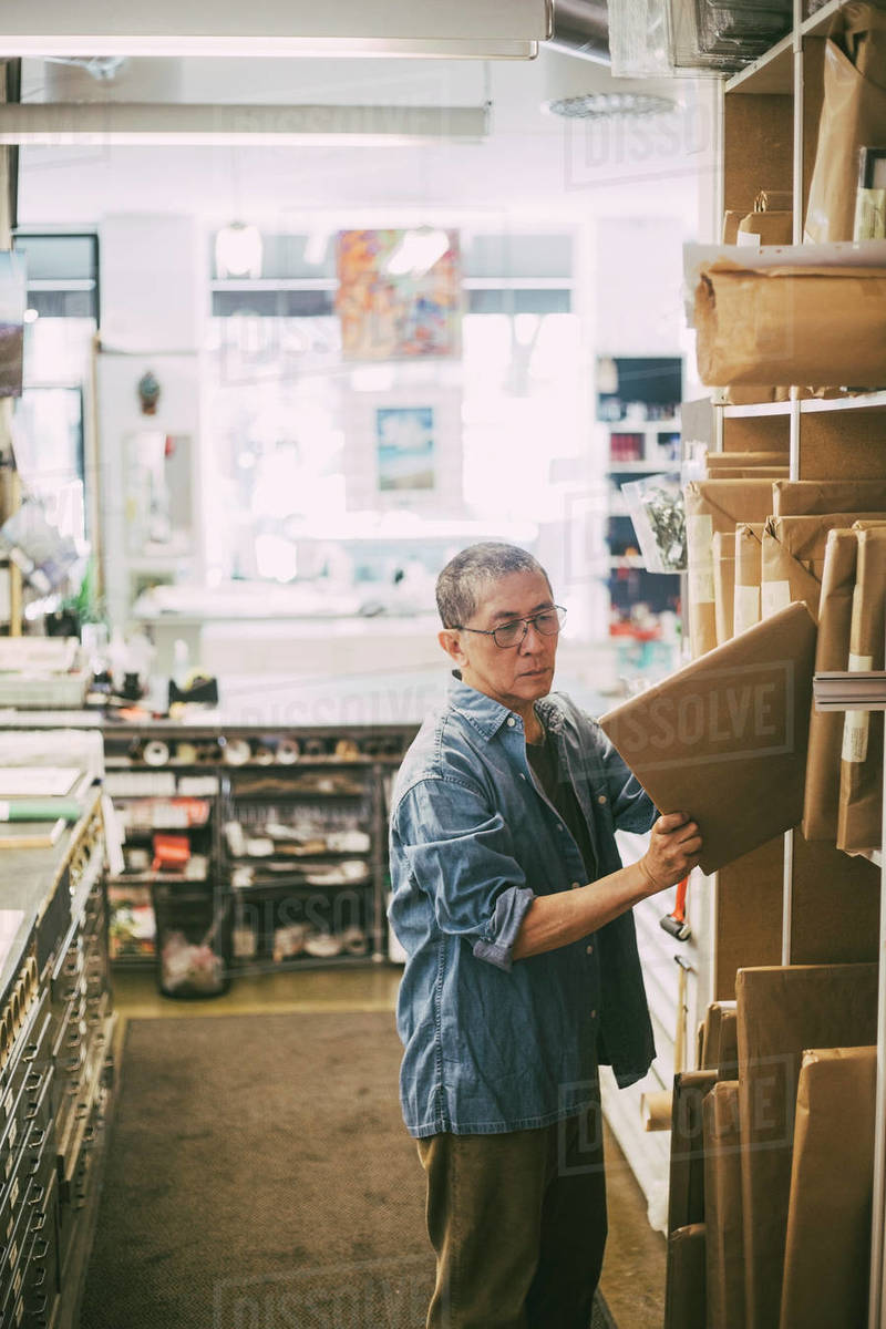 Senior male owner arranging frames in rack at retail shop Stock Photo