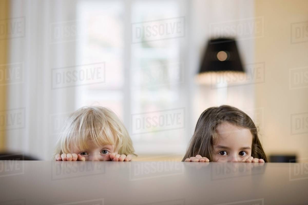 Children looking over table edge Stock Photo Dissolve