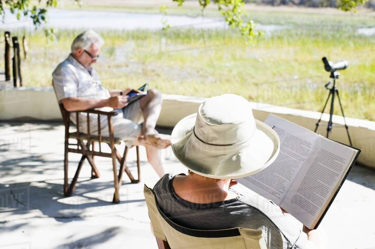 Couple Reading Books At Safari Lodge Kafue National Park Zambia Stock Photo
