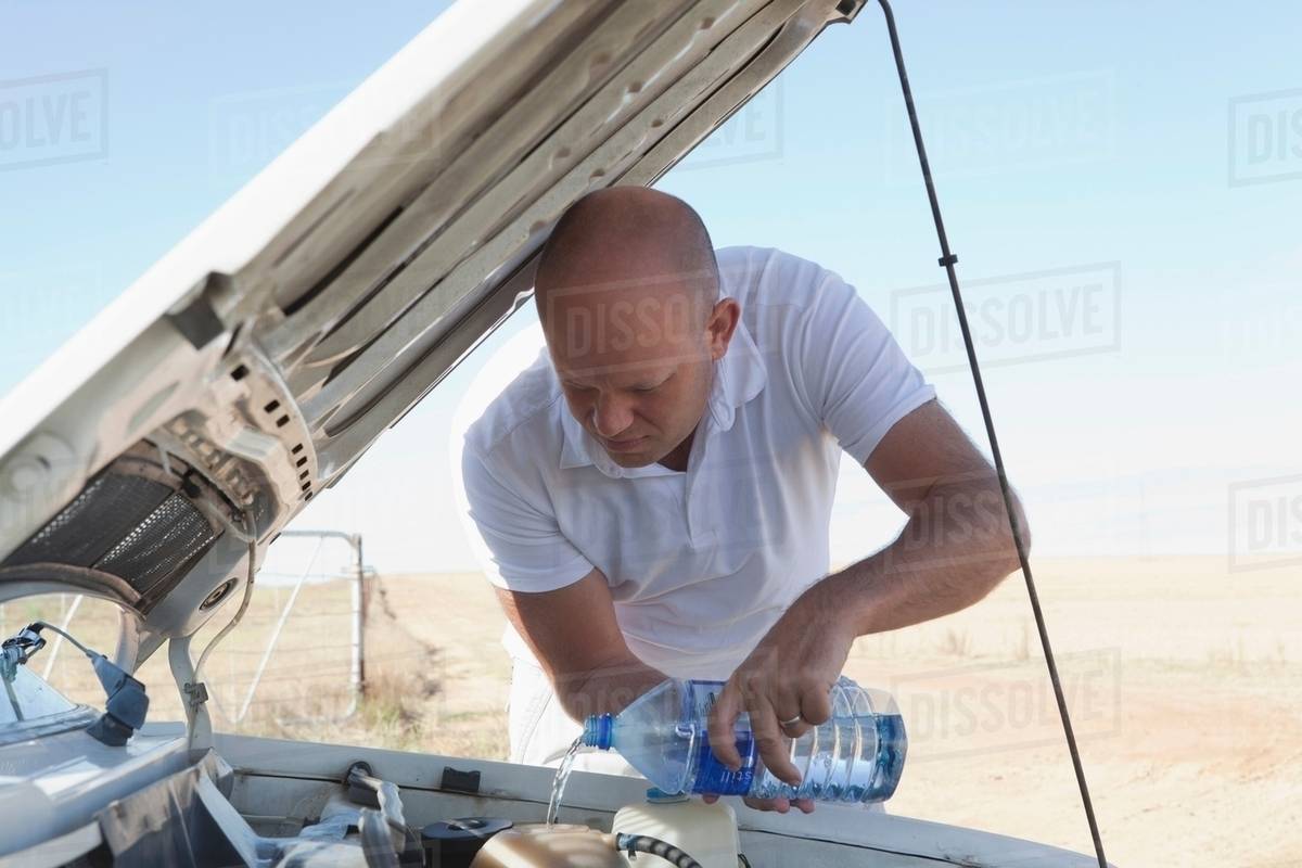 Man pouring water on car engine Stock Photo Dissolve