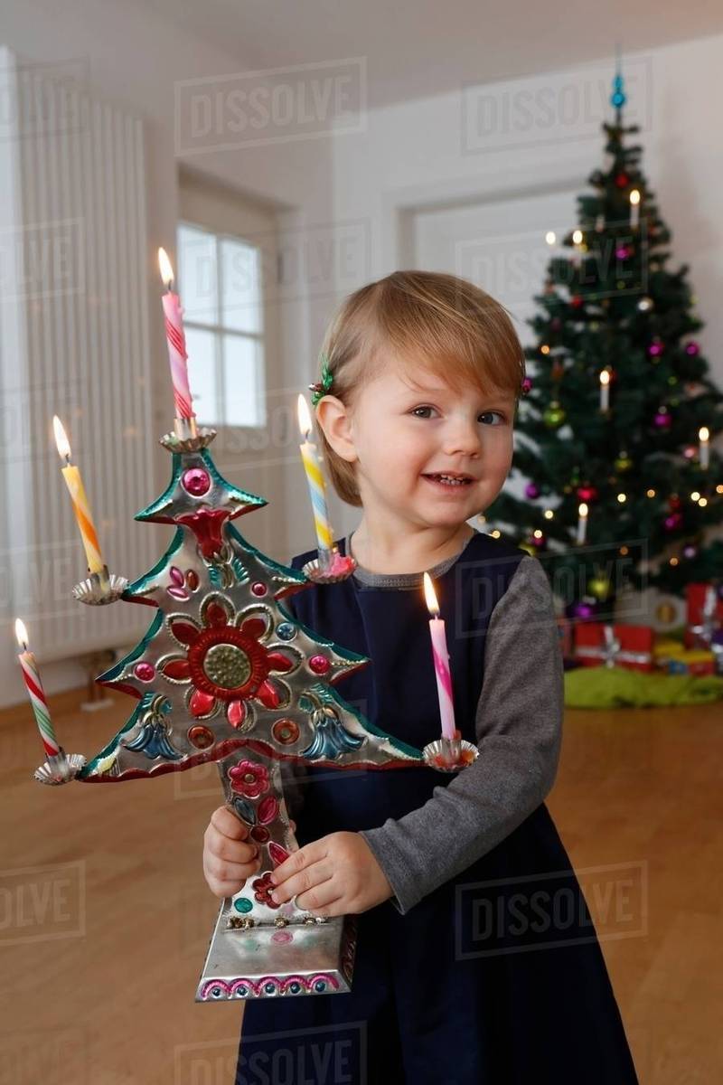 Girl In Front Of Christmas Tree Holding Ornament Looking At Camera Smiling Girl In Front Of Christmas Tree Holding Ornament Looking At Camera Smiling