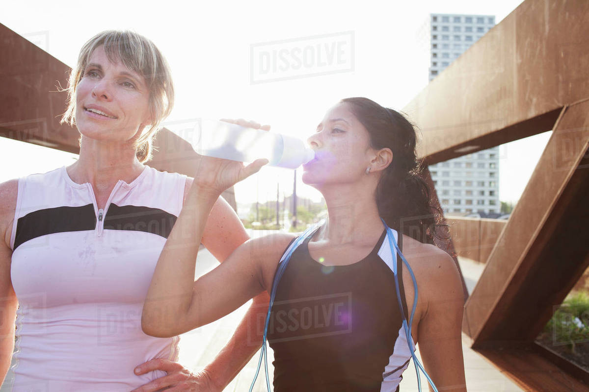 Two women taking a water break from training on urban footbridge
