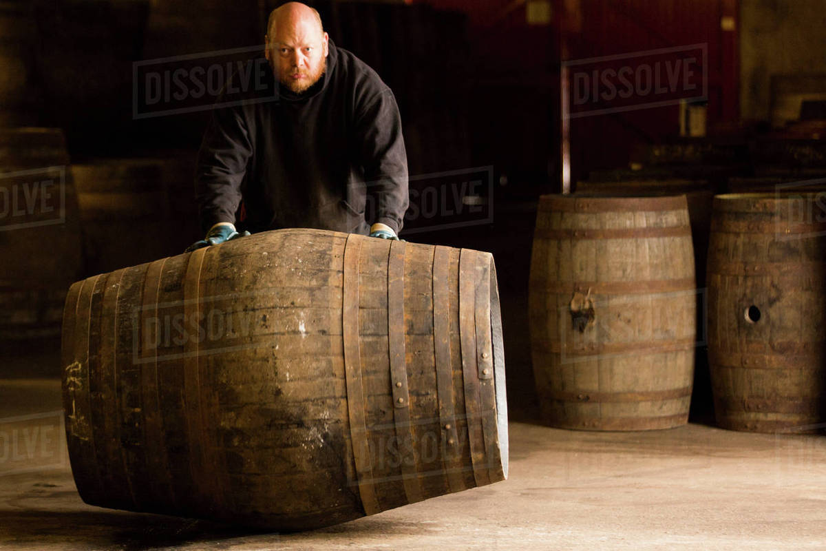 Portrait of worker rolling whisky cask in whisky distillery - Royalty ...