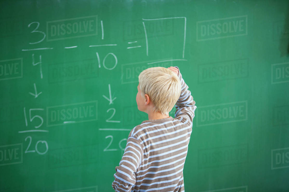 Boy in classroom, working out maths problem on blackboard, rear view