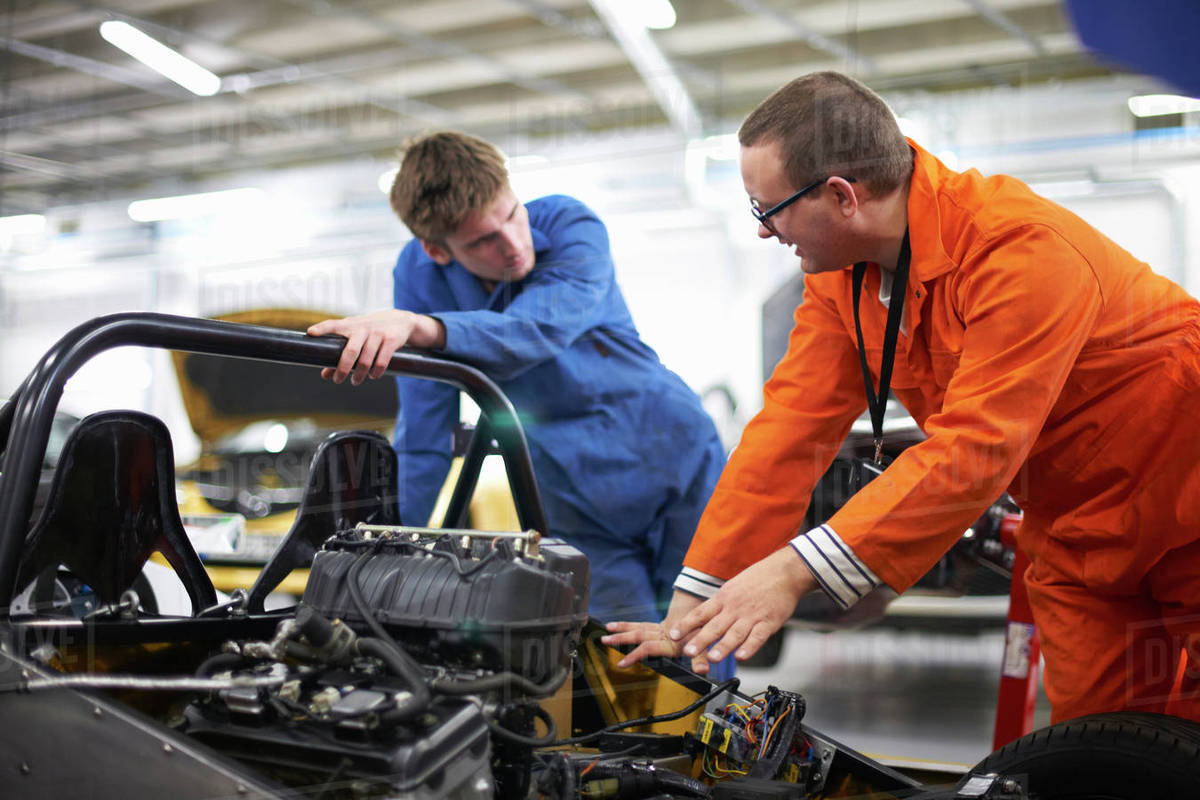 College mechanic students discussing racing car engine in repair garage