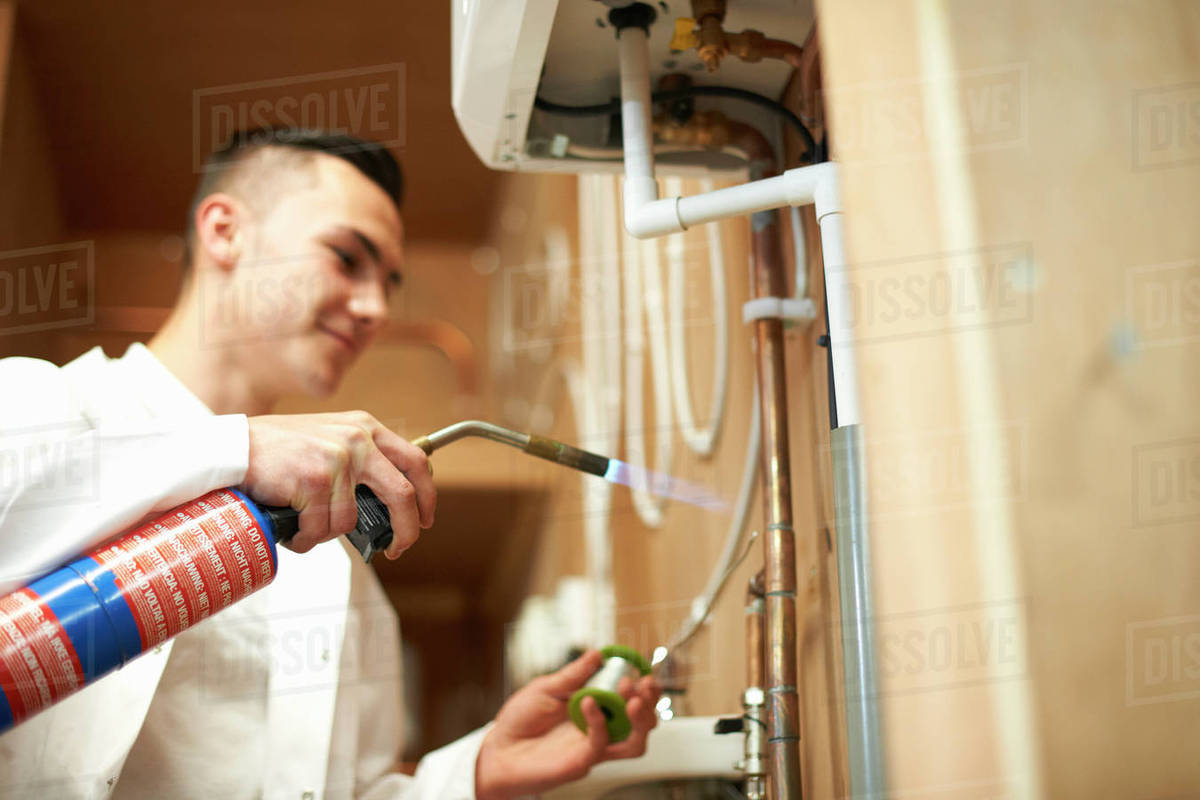 Young male trainee plumber using blow torch on pipework in college