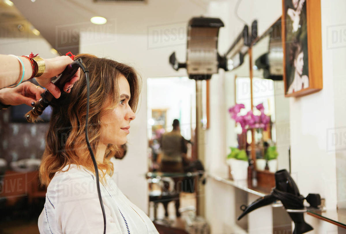 Hairdresser Using Curling Tongs On Customer S Long Brown Hair In