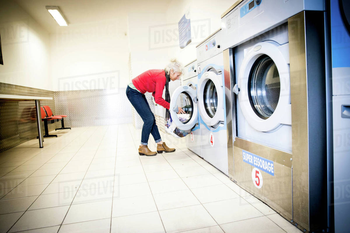 Woman using washing machine in laundrette Stock Photo Dissolve