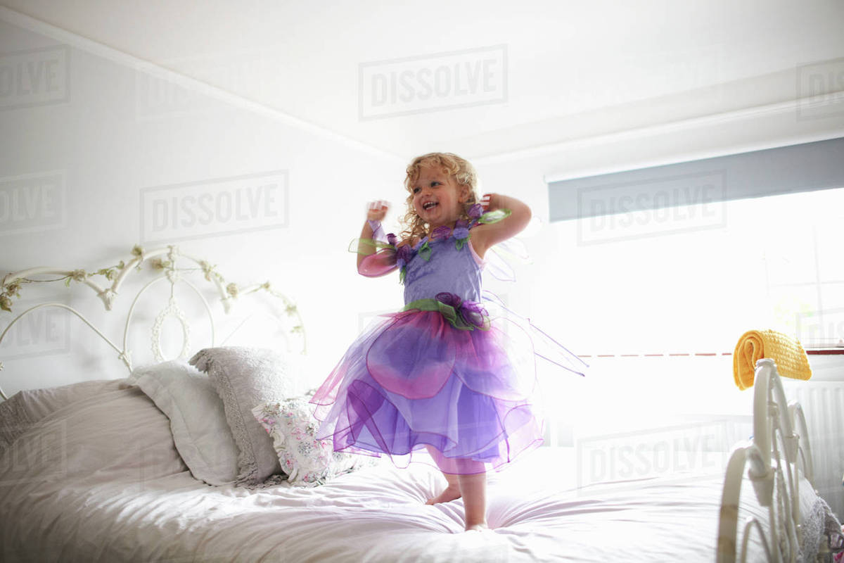 Young girl dressed in fairy costume, standing on bed, smiling Royalty-free stock photo