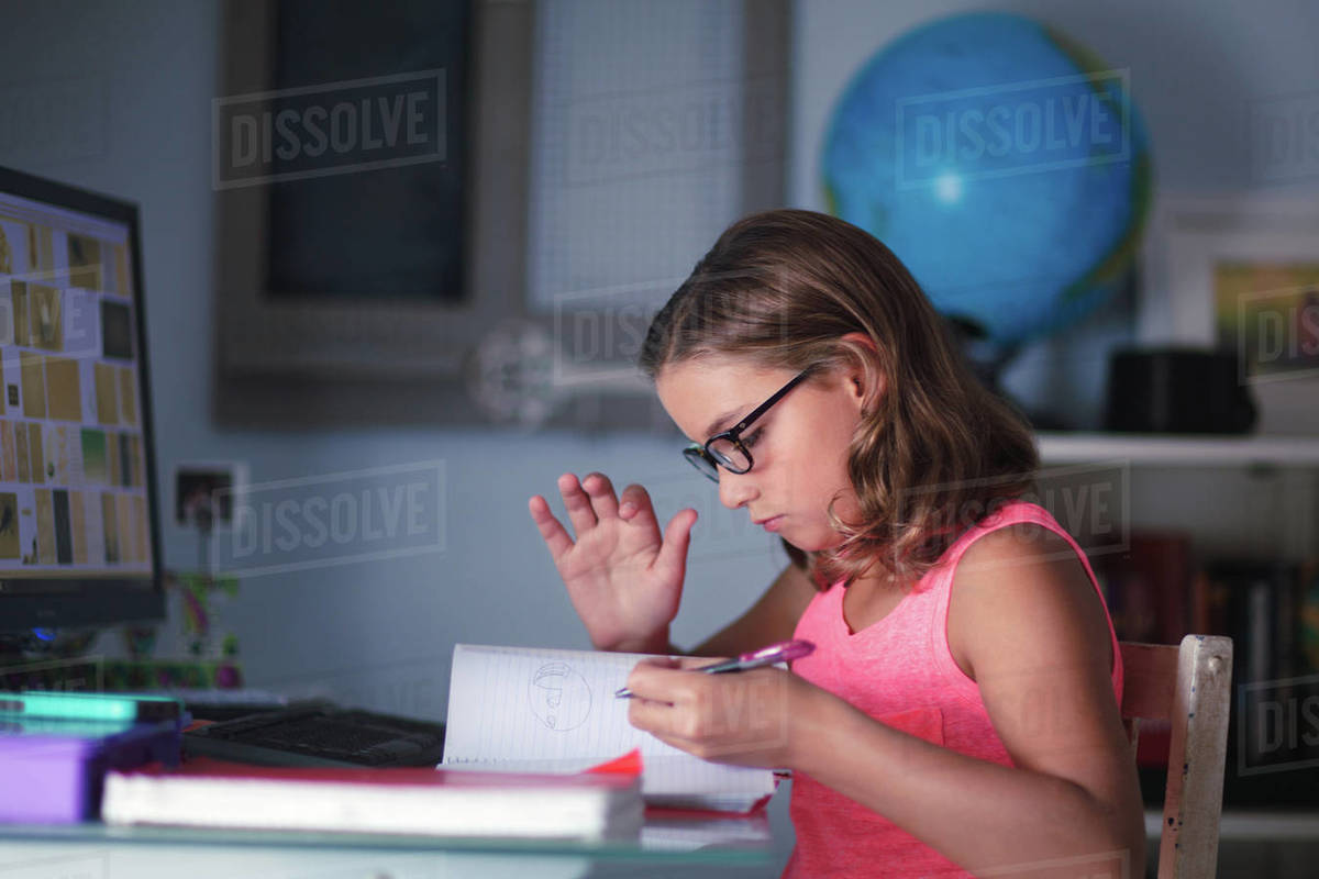 Young girl sitting at desk, doing homework, looking through book ...