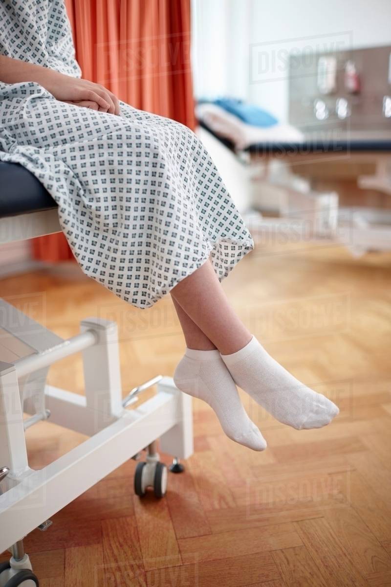 Girl sitting on hospital bed, wearing examination gown Stock Photo