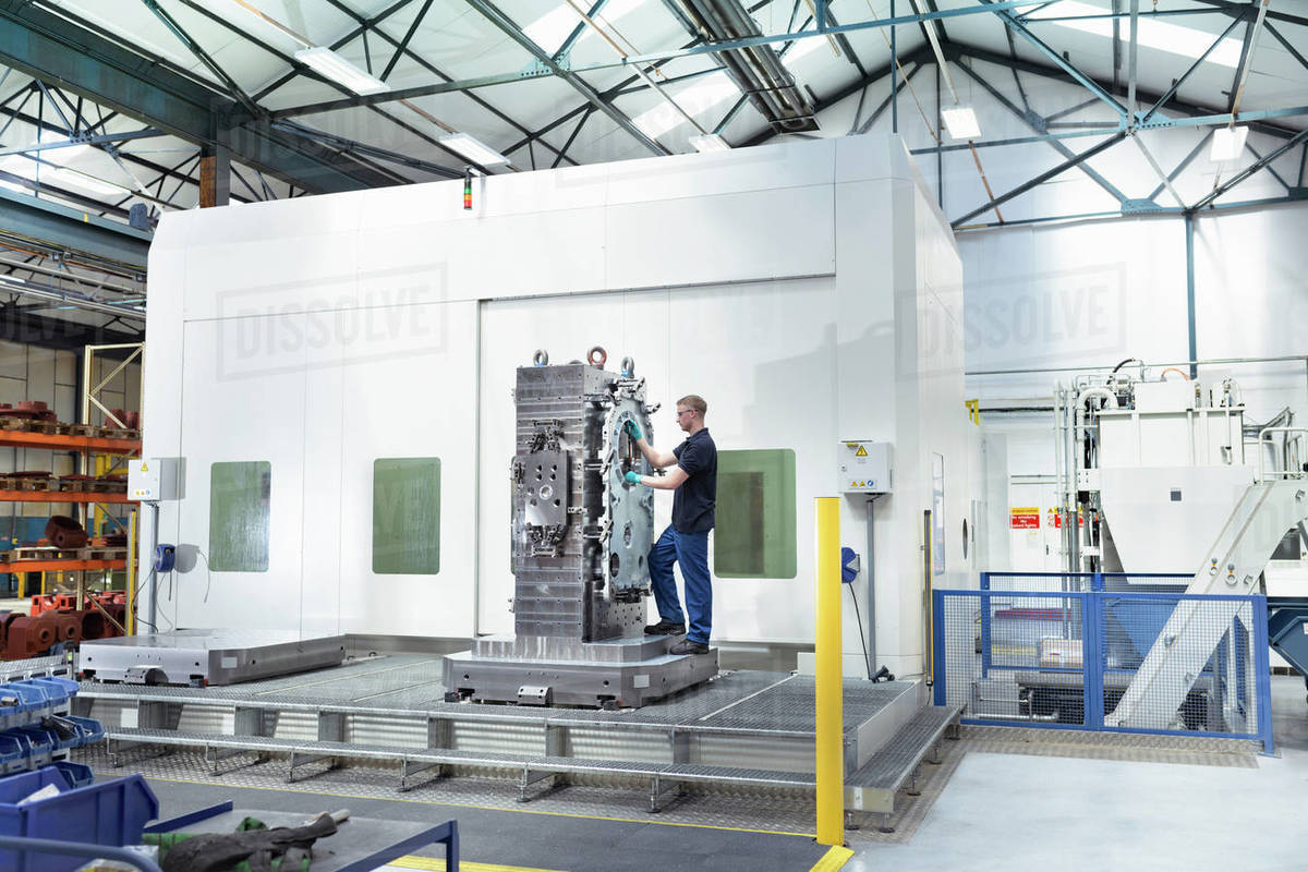Apprentice engineer setting up large CNC machine in gearbox factory