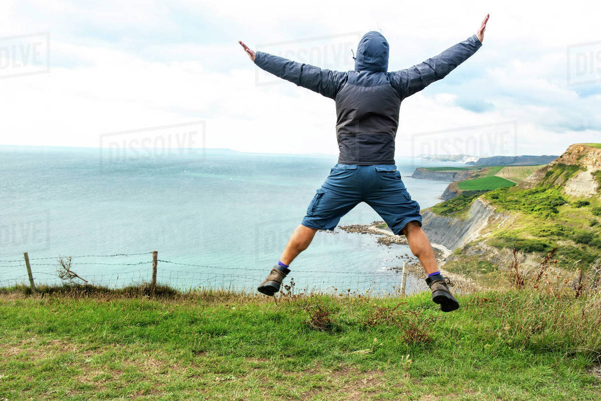 Man jumping on clifftop by sea, Bournemouth, UK Stock Photo Dissolve