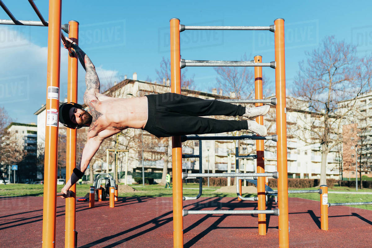 Man using horizontal ladder in outdoor gym Stock Photo Dissolve