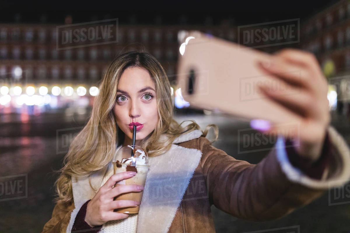 Young woman drinking frappe coffee and taking selfie on city street at night, Madrid, Spain Royalty-free stock photo