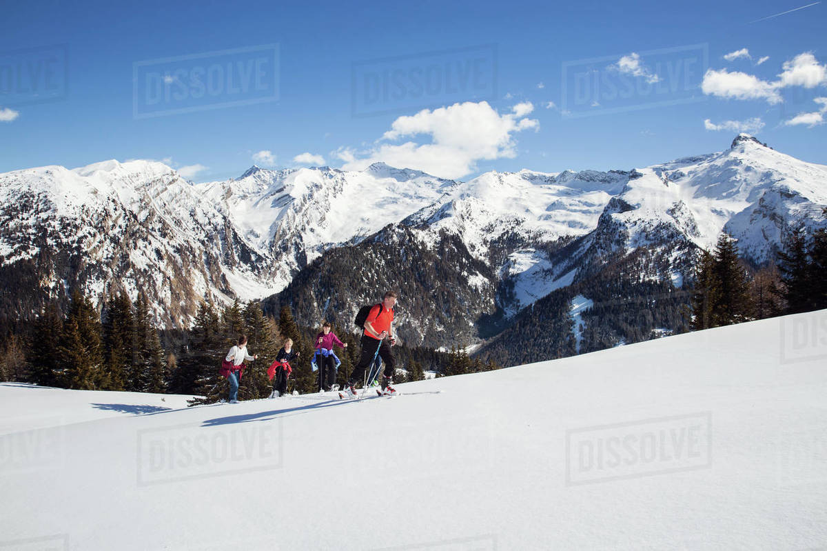 Mature couple and daughters snowshoeing uphill in snow covered mountain