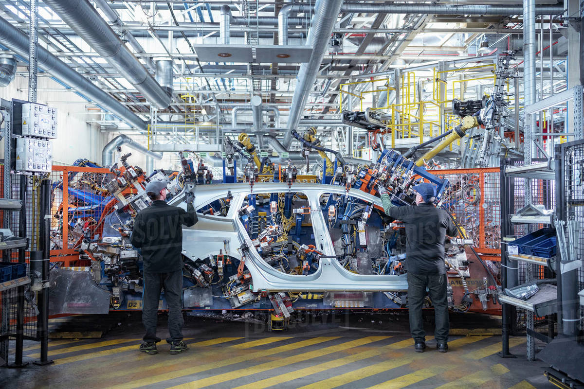 Workers loading car body spot welding machine with robots in car factory Royalty-free stock photo