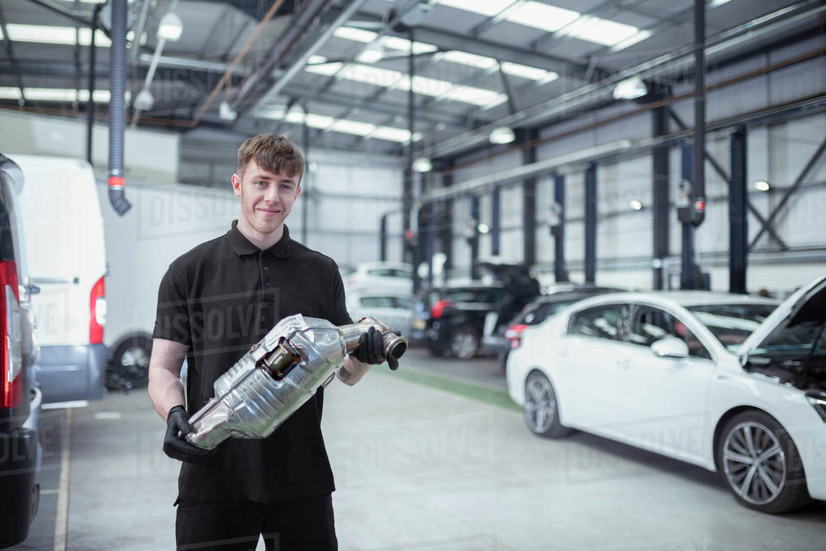 Portrait of apprentice engineer holding catalytic converter in car service centre Royalty-free stock photo