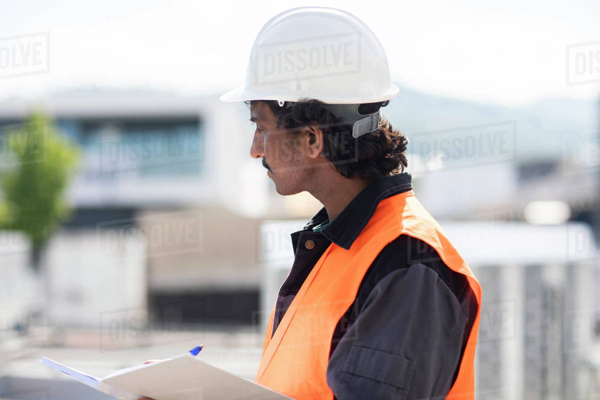 Male engineer outside industrial building writing in notebook, side view Royalty-free stock photo