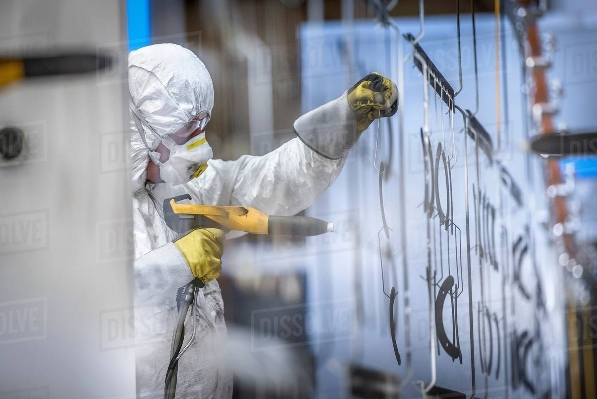 Worker powder coating parts in paint spray booth in sheet metal factory