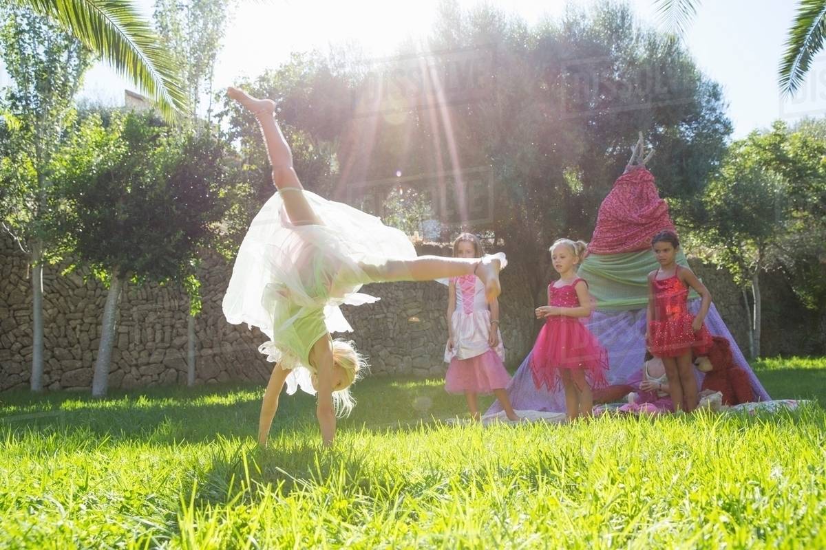 Girls watching friend in fairy costume doing cartwheel in garden Royalty-free stock photo