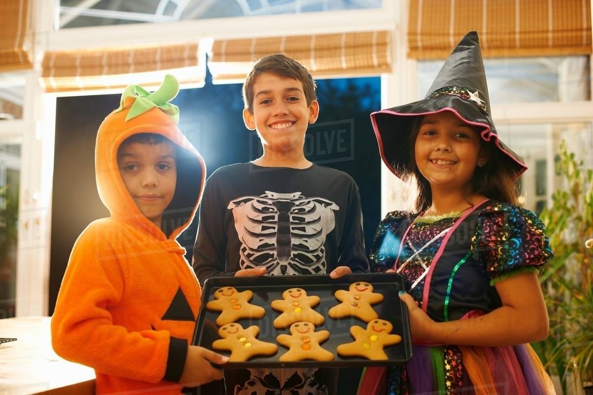 brothers and sister wearing halloween costumes holding tray of gingerbread men