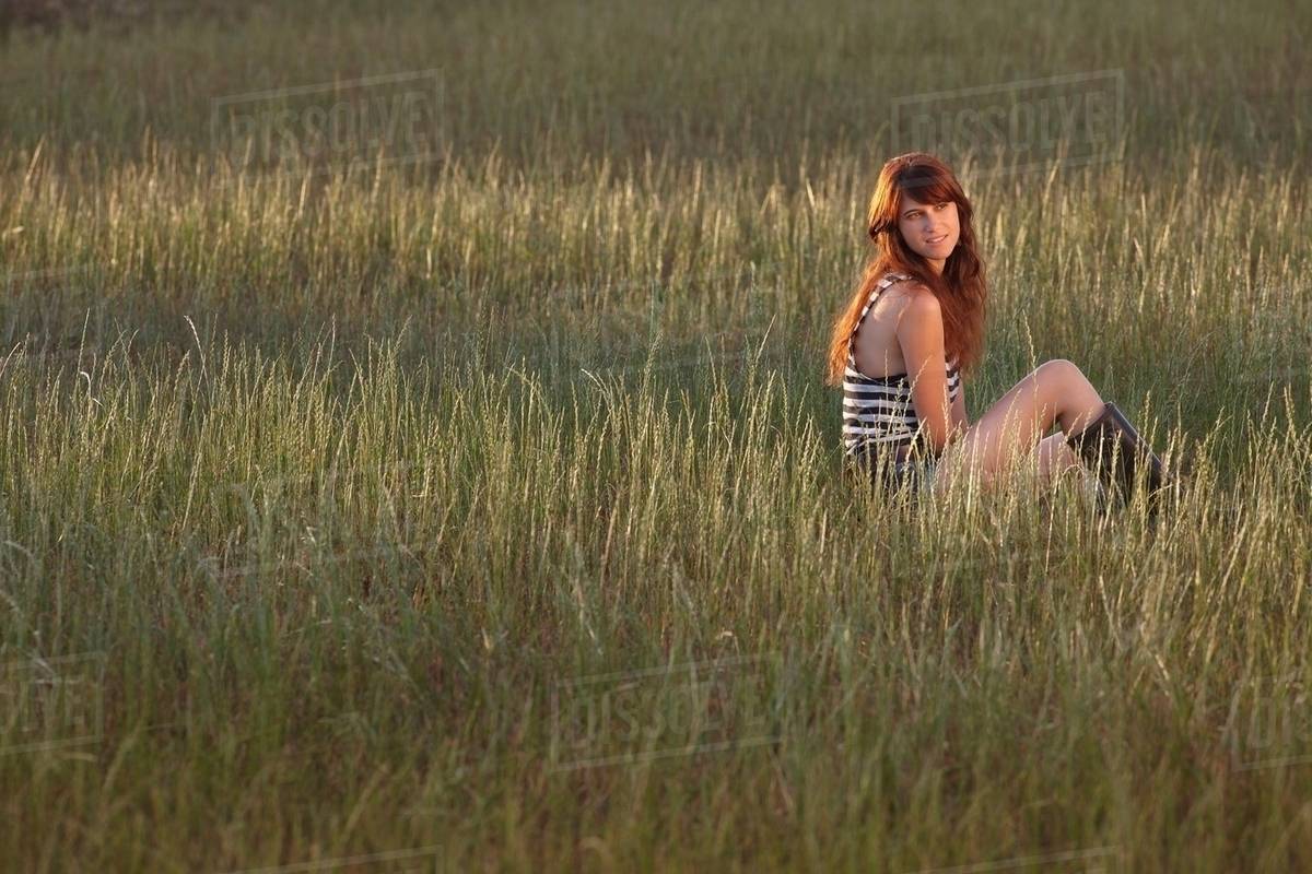 Woman sitting in grassy field Stock Photo Dissolve