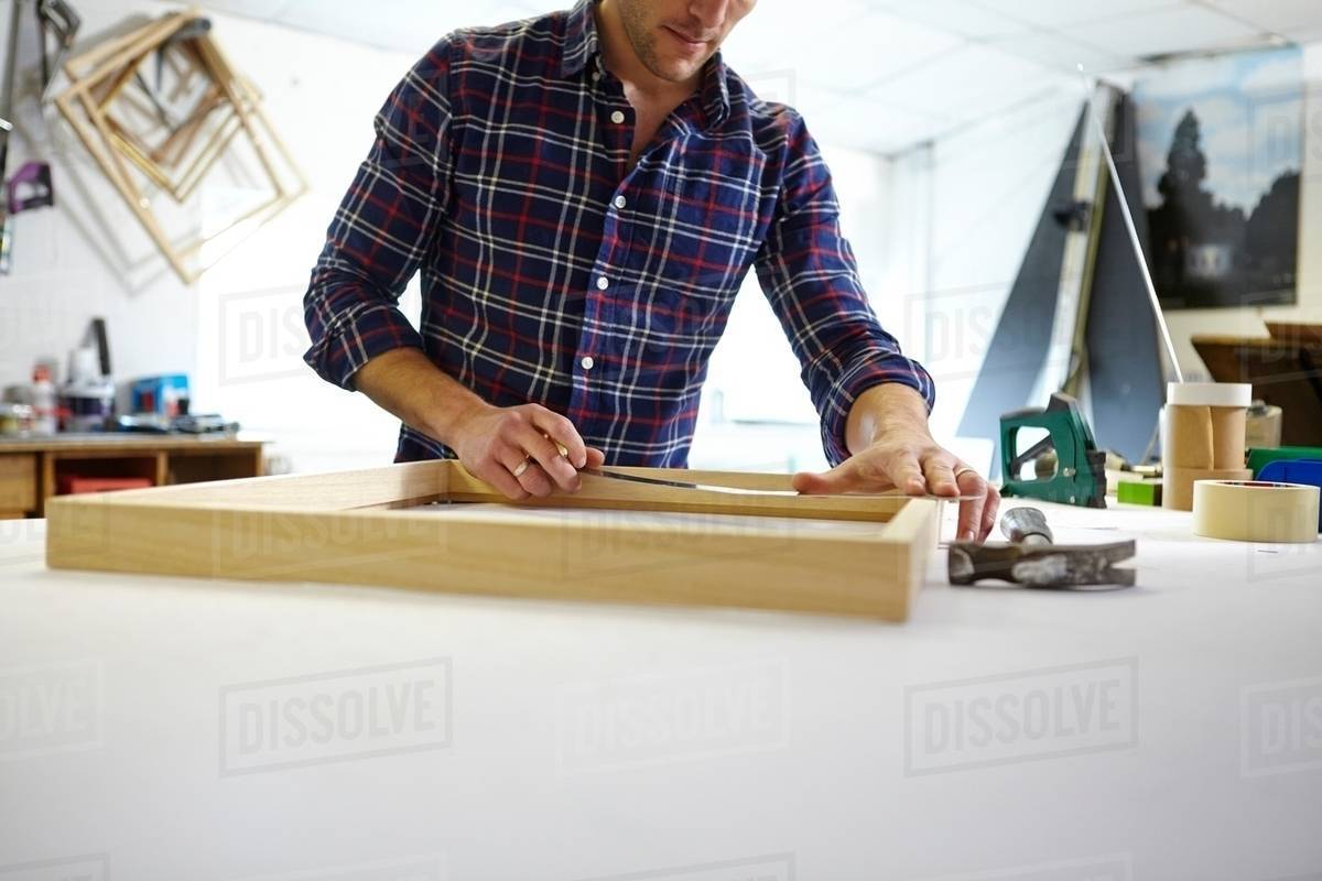 Mid adult man measuring frame on workbench in picture framers Stock Photo Dissolve