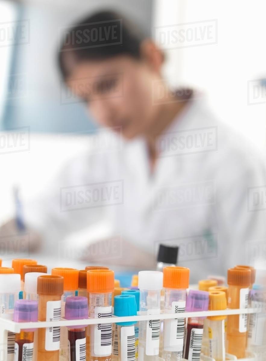 Female doctor making notes on blood and urine samples at desk Stock