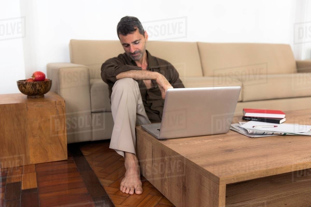 Barefoot Mature Man Sitting On Wooden Floor With Laptop Looking