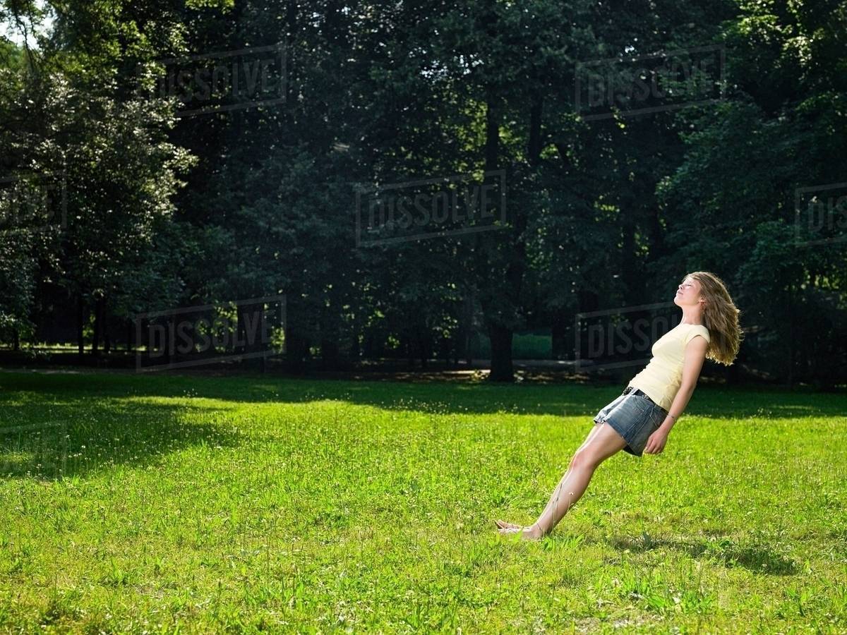 Young woman in park free falling backwards with eyes closed Stock