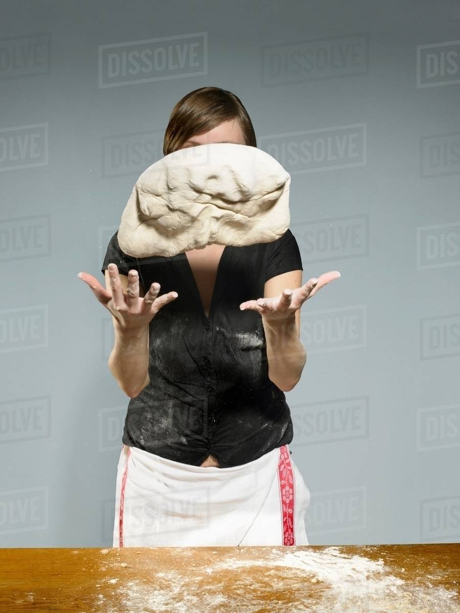 Studio portrait of young woman throwing bread dough mid air Stock