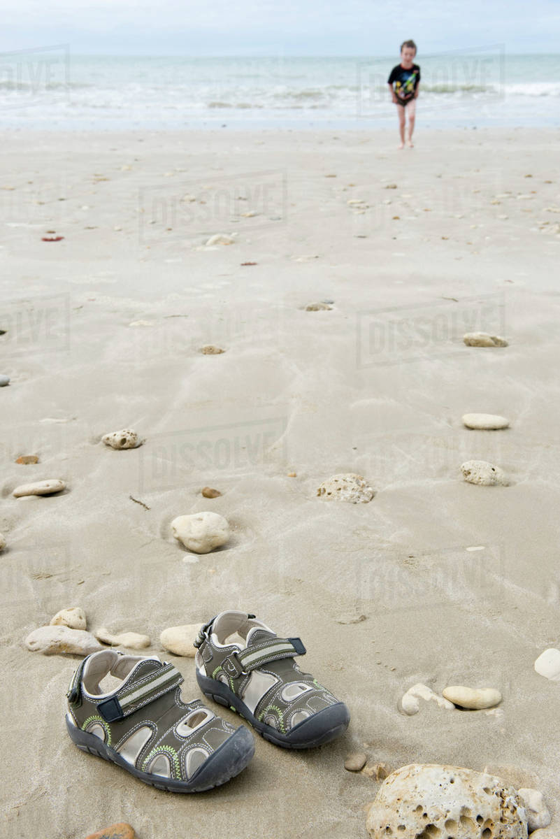 Boy At The Beach Focus On Sandals In Foreground Stock Photo Boy At The Beach Focus On Sandals In Foreground