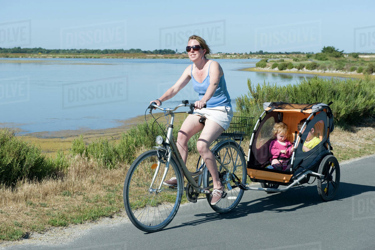 Woman riding along bicycle path with children in bicycle trailer Royalty-free stock photo