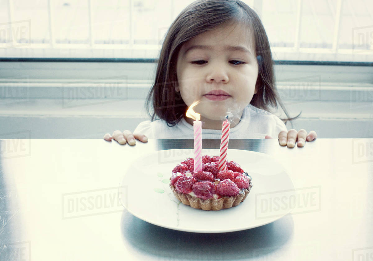 Little girl blowing out candles on birthday cake Stock Photo Dissolve