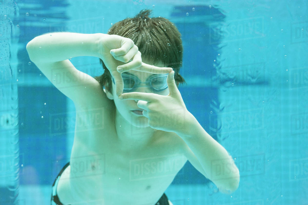 Boy swimming underwater in swimming pool, hands forming finger frame