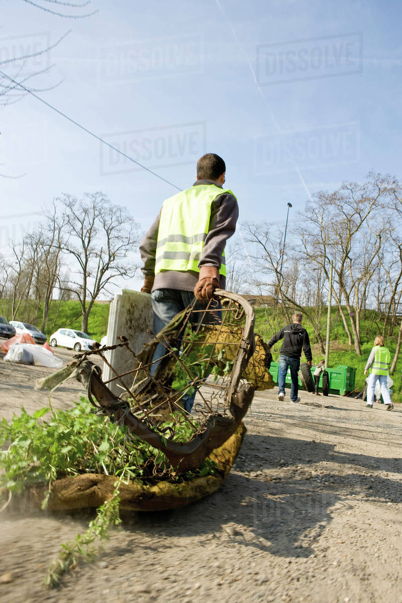 Volunteer carrying rusty mattress to dumpster Stock Photo Dissolve