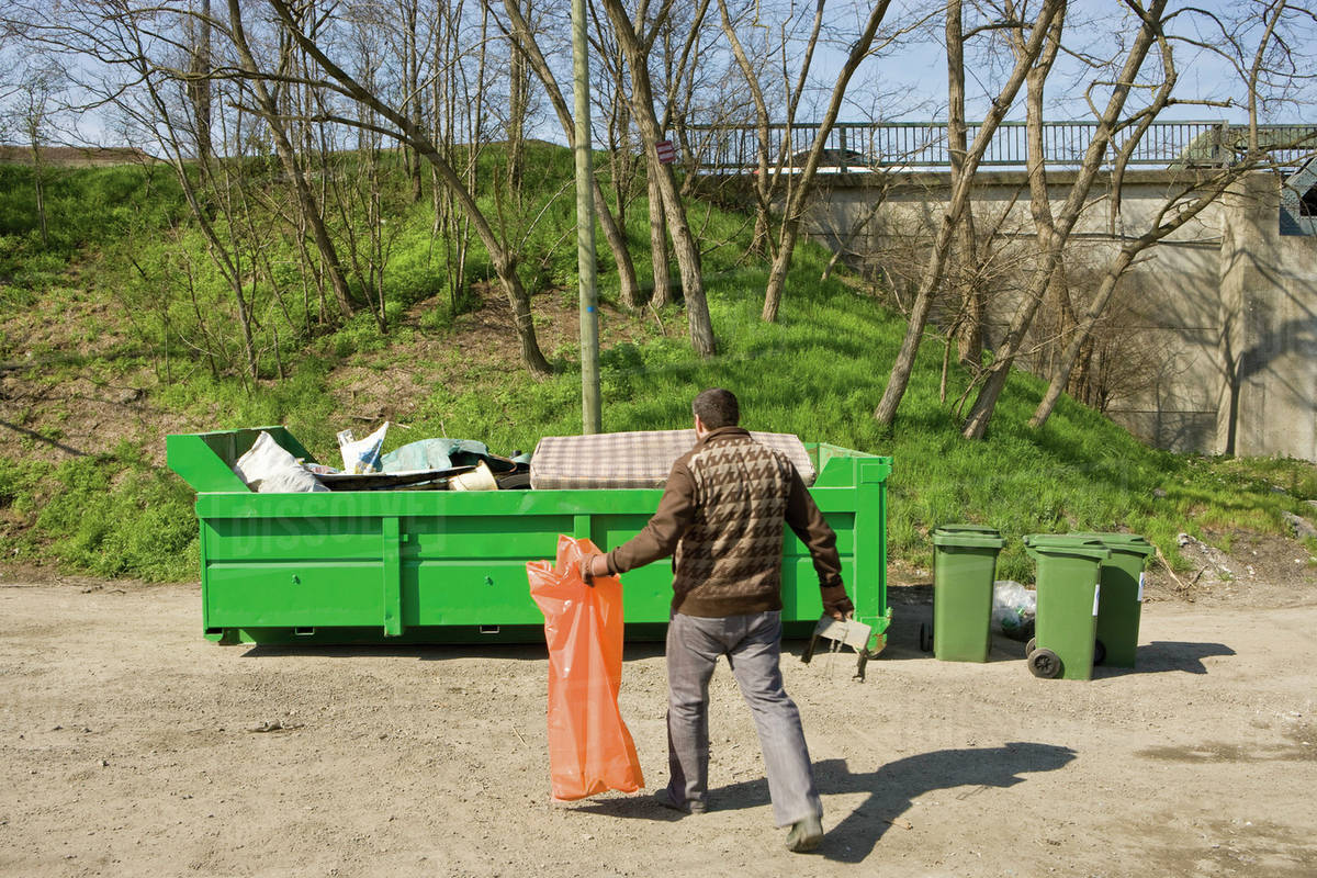Man taking garbage to dumpster Stock Photo Dissolve