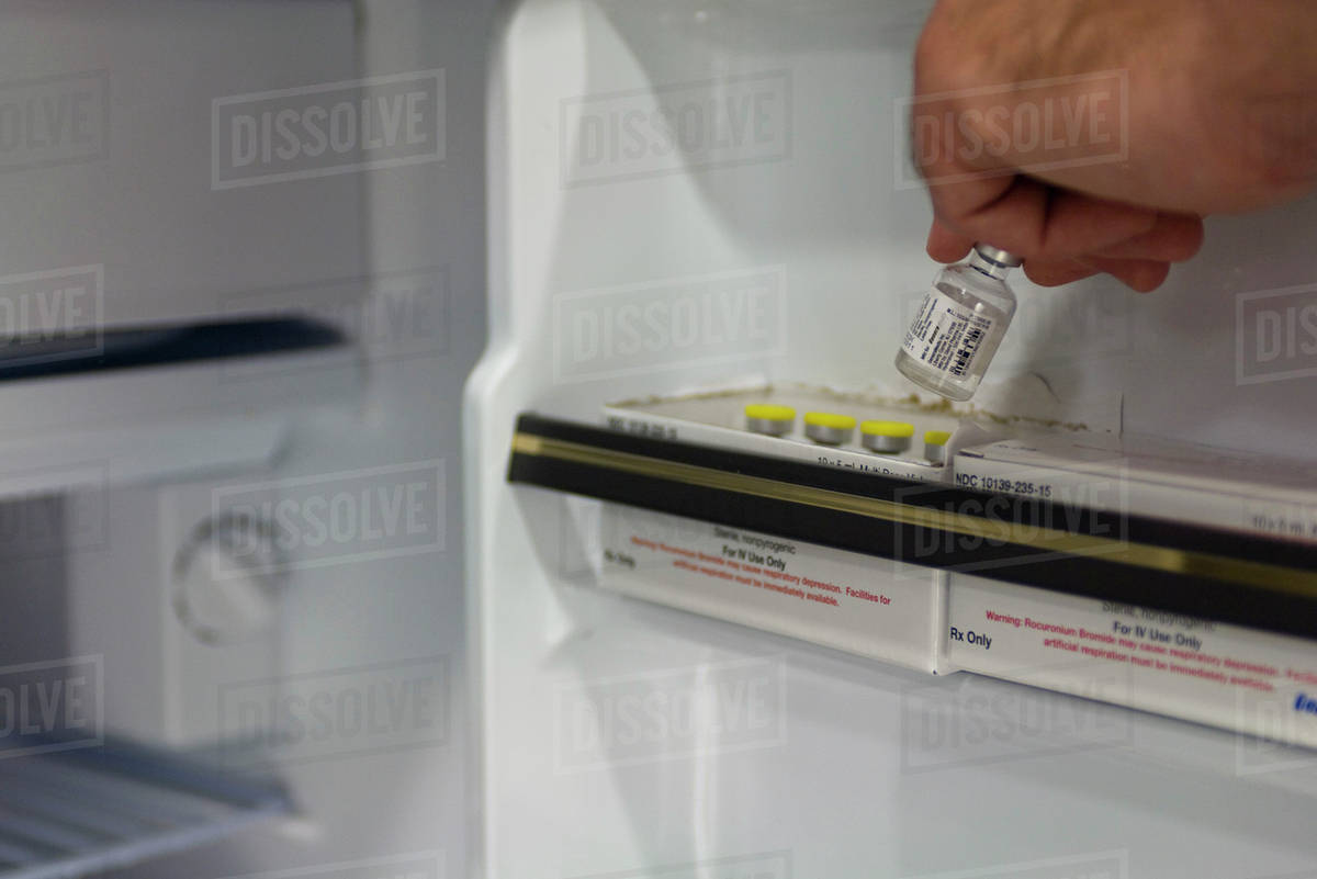 Healthcare professional removing medication vial from refrigerator