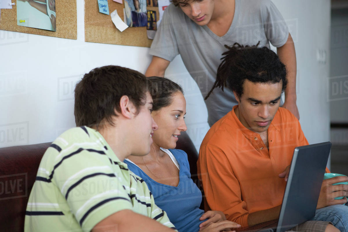 College students gathered around classmate using laptop computer