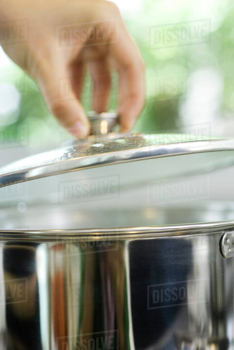 Person removing lid from cooking pot Stock Photo Dissolve