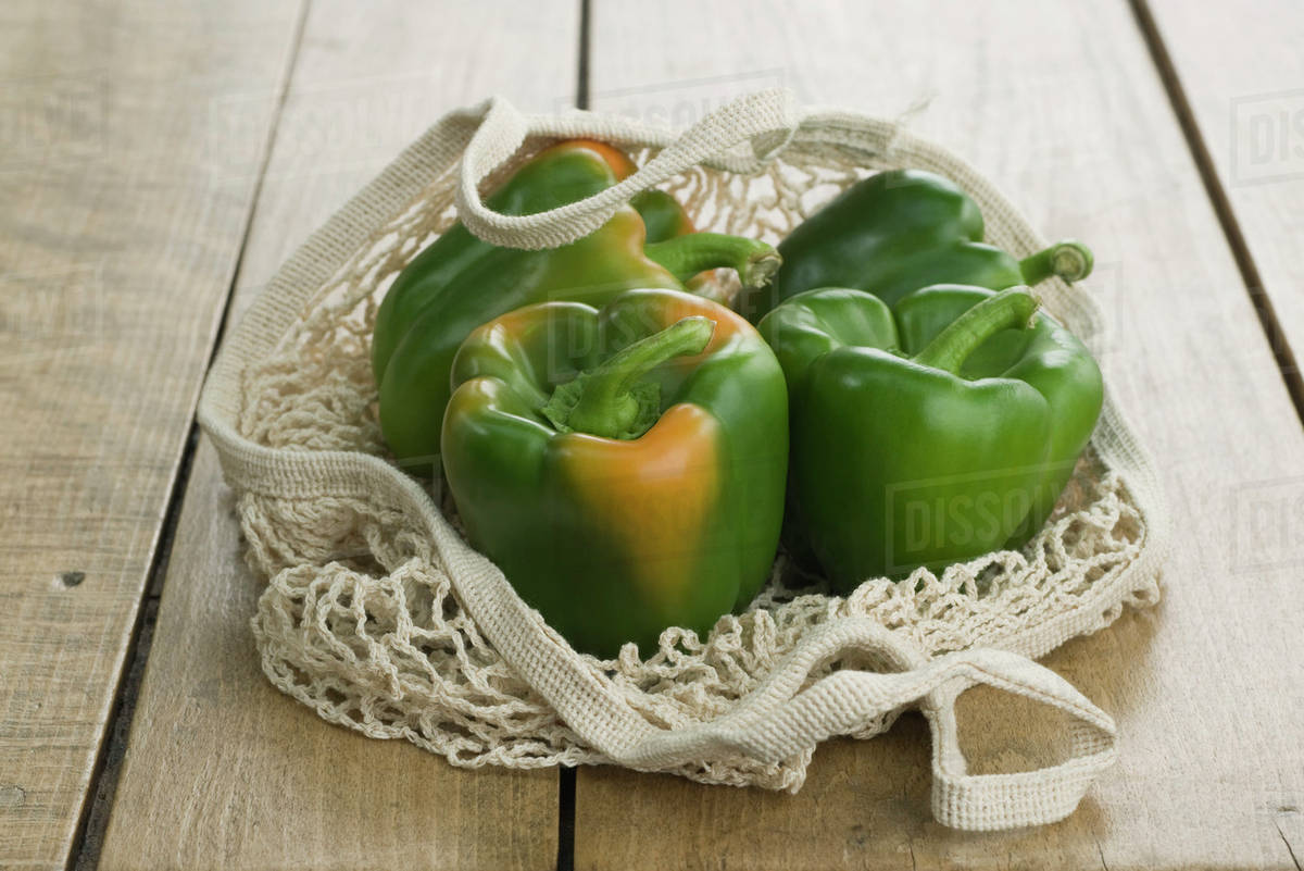 Fresh green bell peppers in mesh shopping bag Stock Photo Dissolve