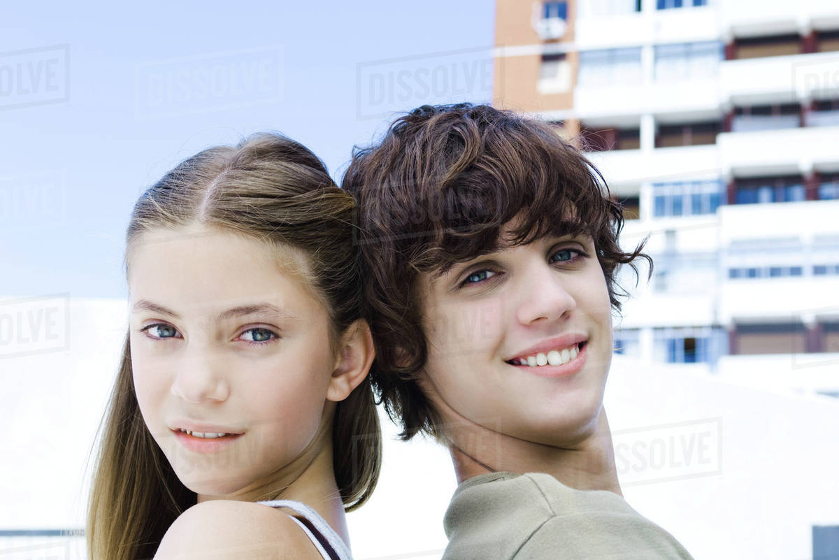 Two young friends back to back, smiling at camera, side view - Royalty ...