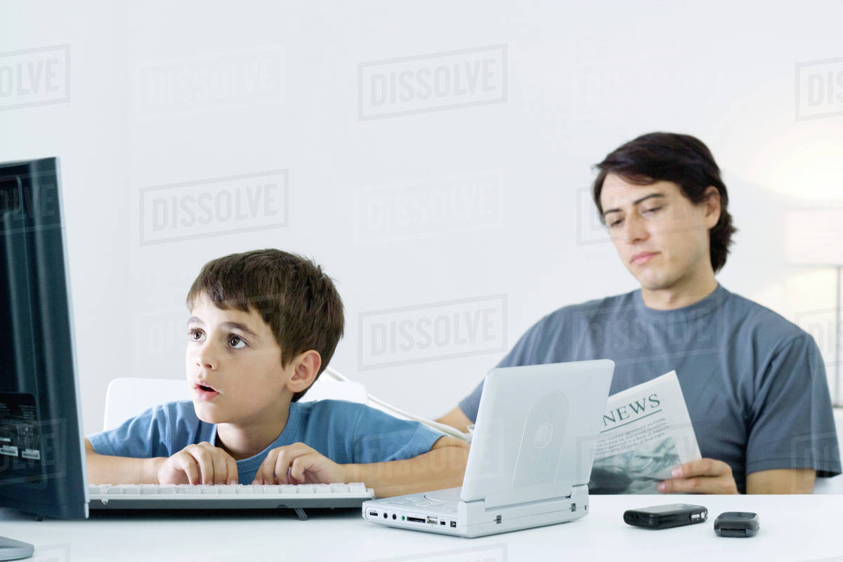 Little Boy Computer And Portable Dvd Player Father Reading Newspaper In Background Stock Photo Dissolve