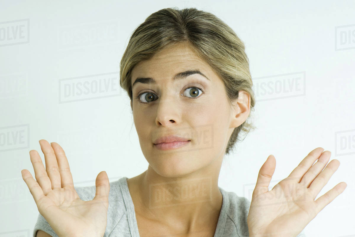 Young woman raising eyebrows, holding up palms, portrait Stock Photo Dissolve