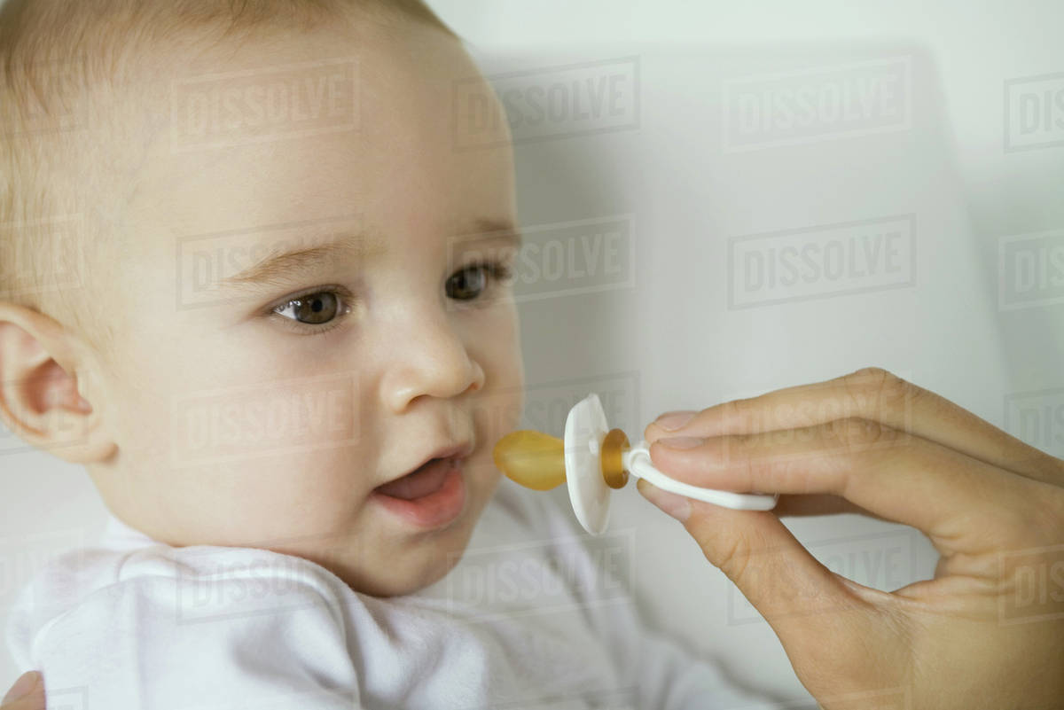 Mother's hand holding up pacifier for baby Stock Photo Dissolve