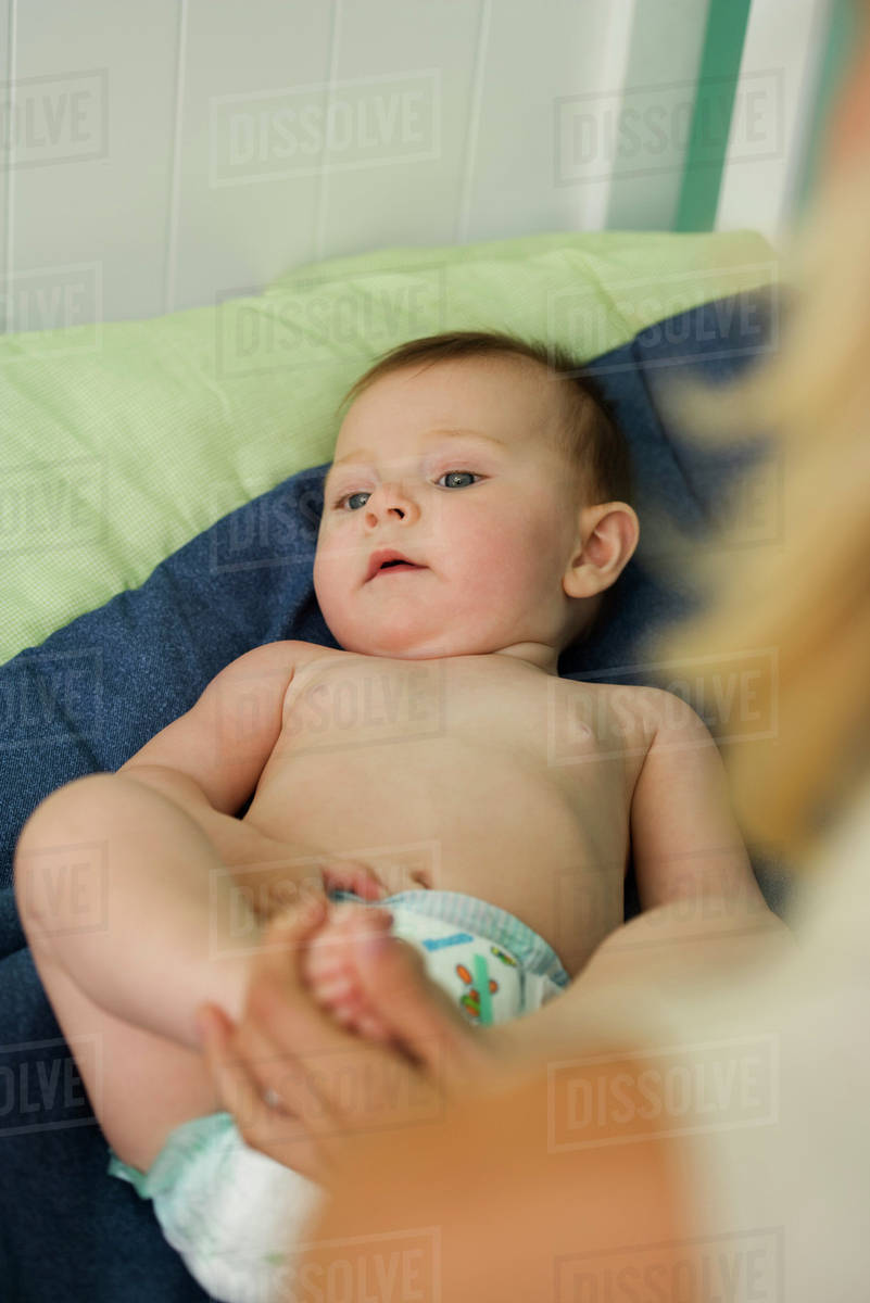 Baby lying in crib, mother holding baby's foot, cropped view Stock