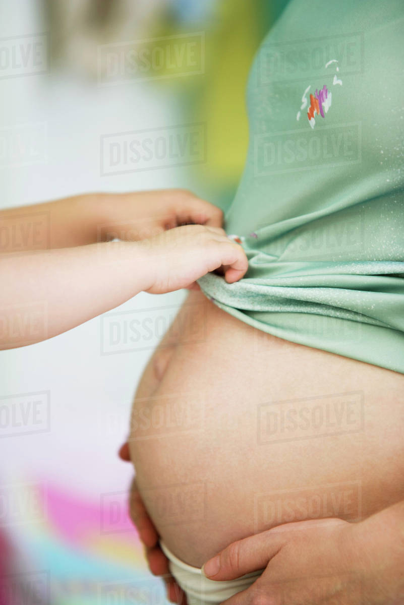 Child pulling mother's shirt down over pregnant belly Stock Photo Dissolve