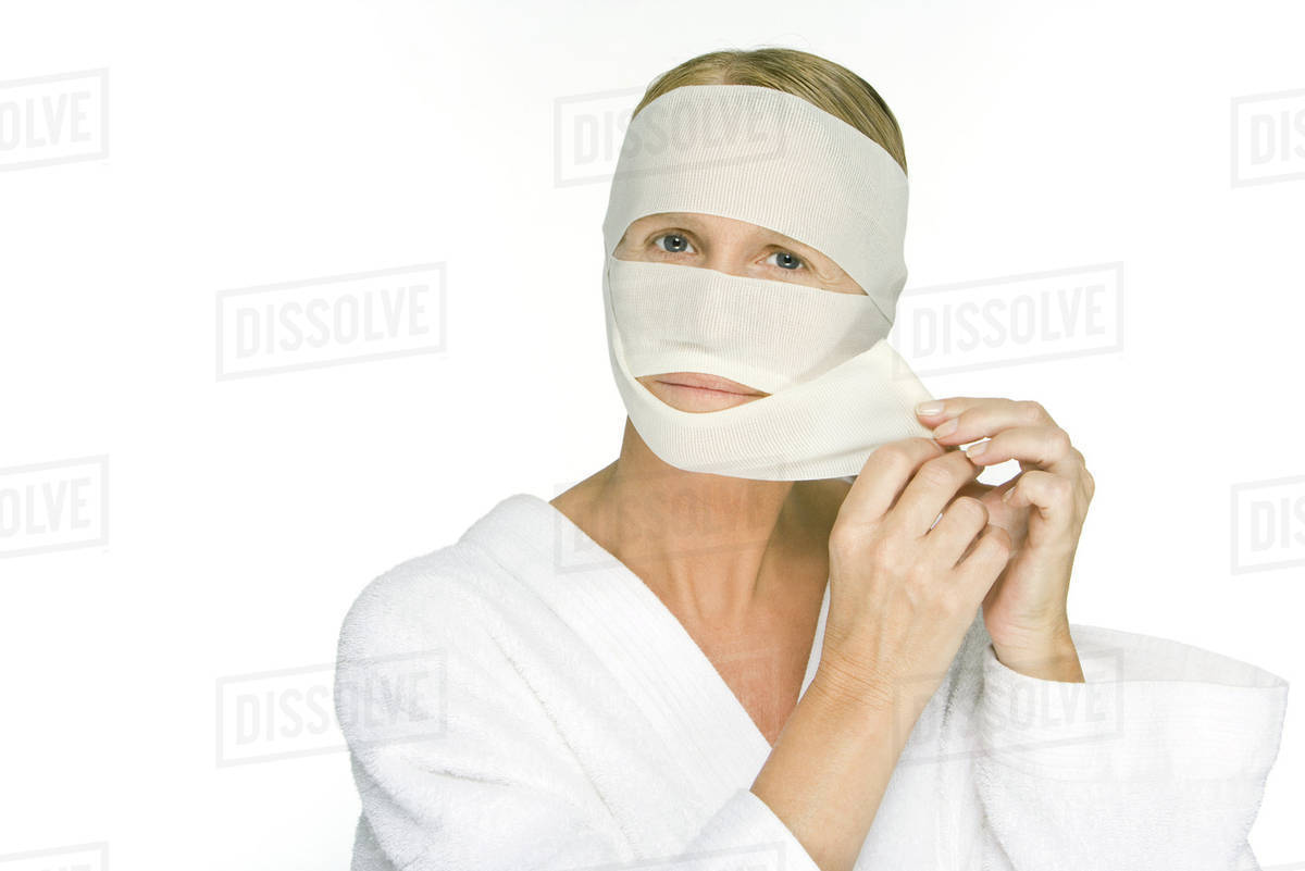 Woman removing bandages from face, looking at camera Stock Photo
